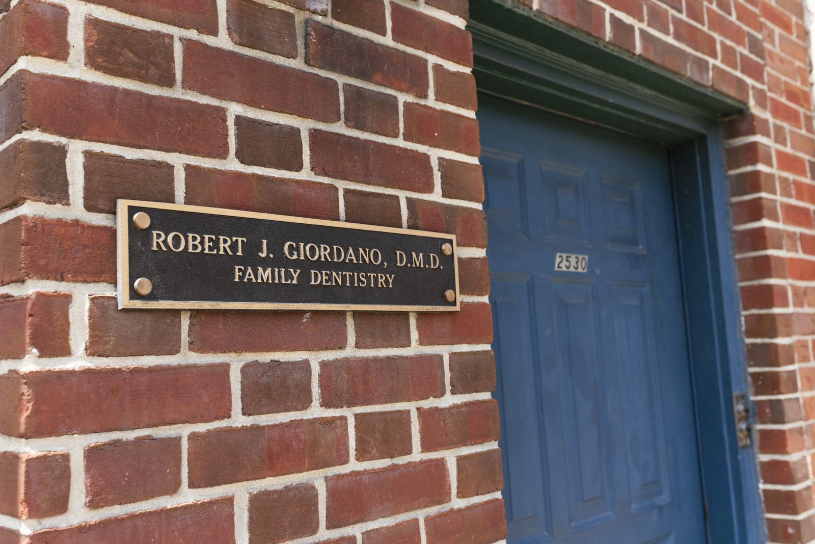 The brass Robert J. Giordano, D.M.D. Family Dentistry plaque beside the blue front door