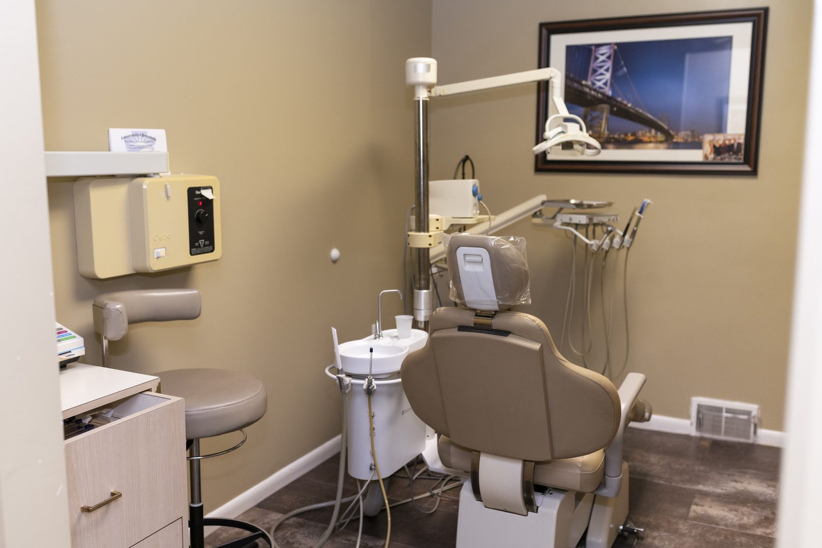 A treatment room with the chair, x-ray arm, and a framed print of the Ben Franklin Bridge