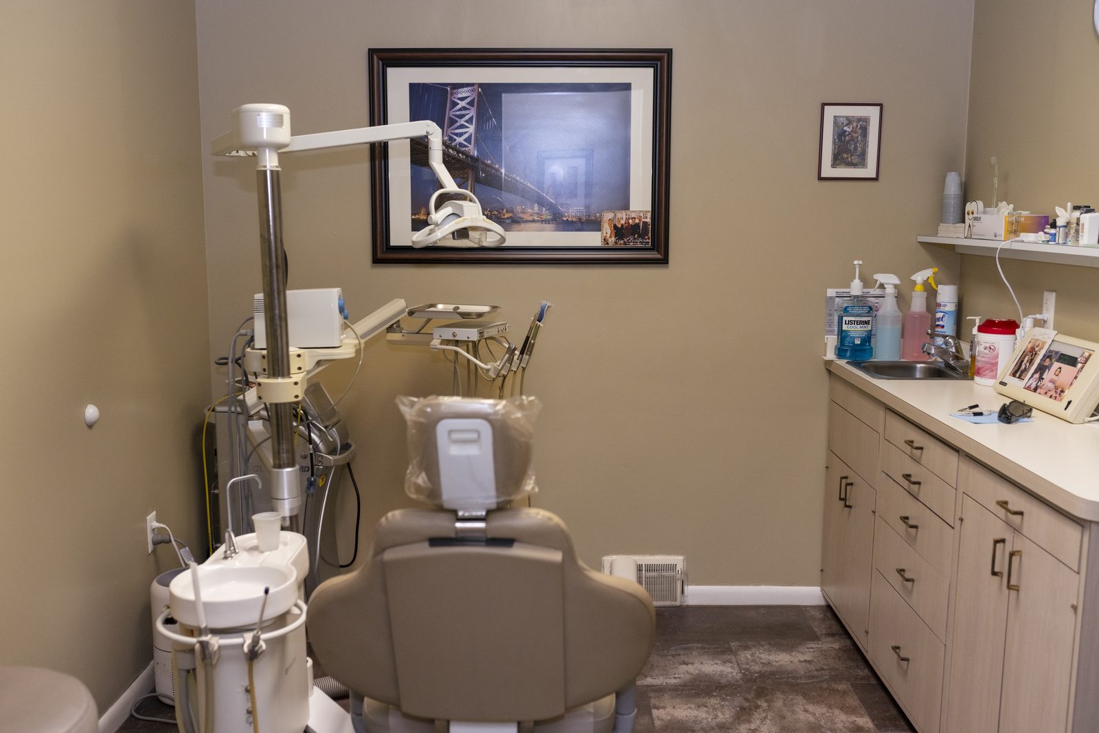 A treatment room with the dental chair, overhead light, and supply counter